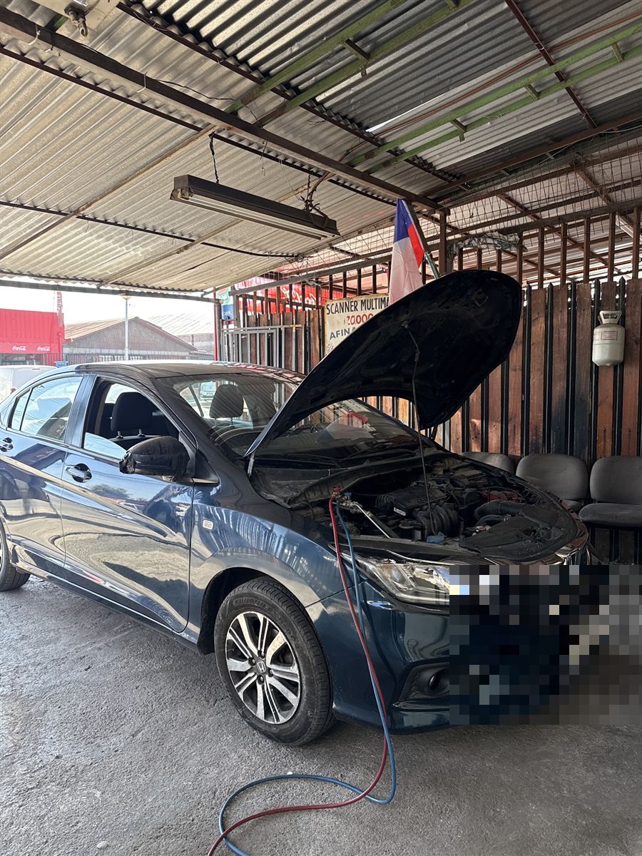 Auto con el capó abierto conectado al equipo de aire acondicionado en el taller